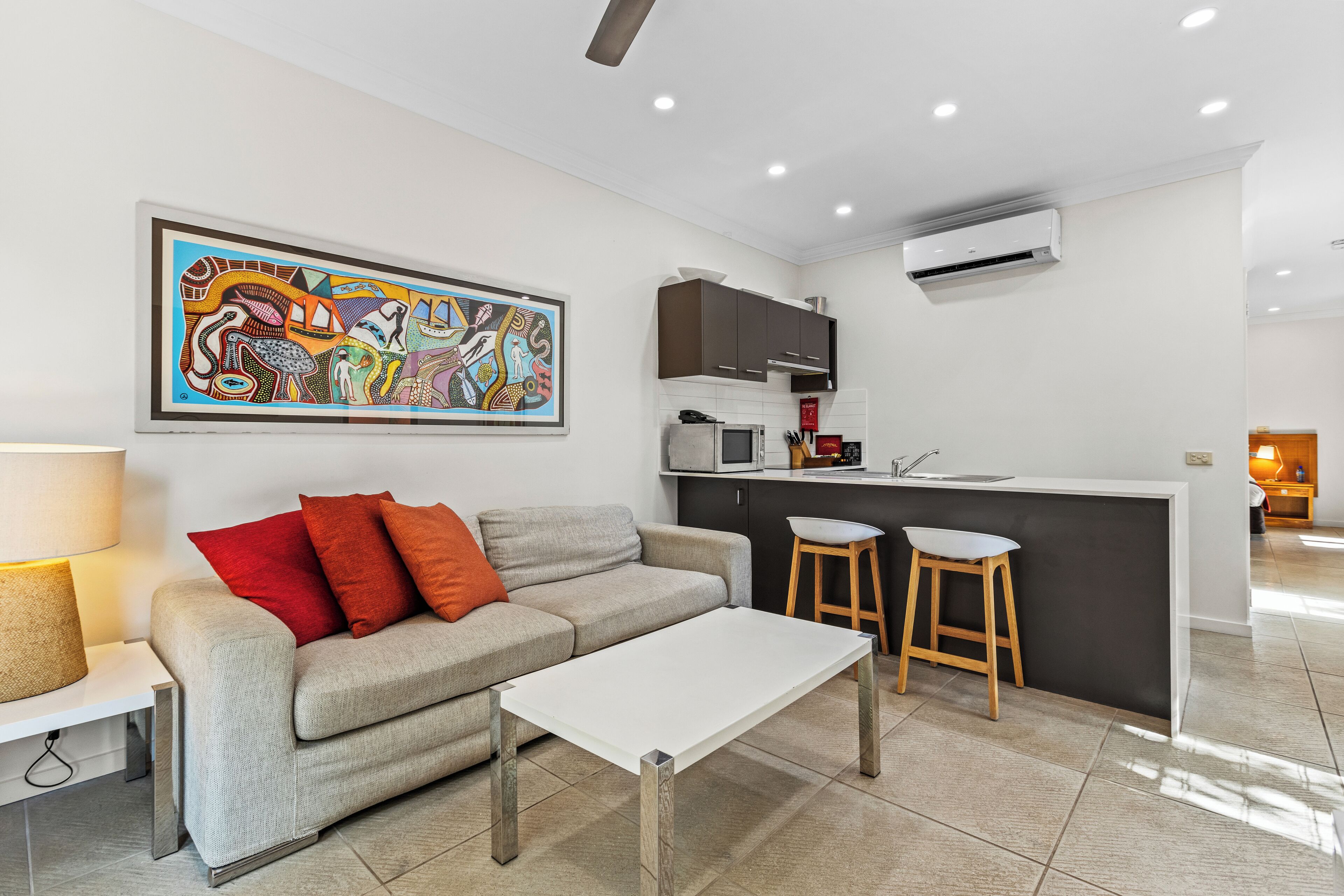 A modern living room with a sofa, a coffee table, and a kitchen area with a bar counter and stools.
