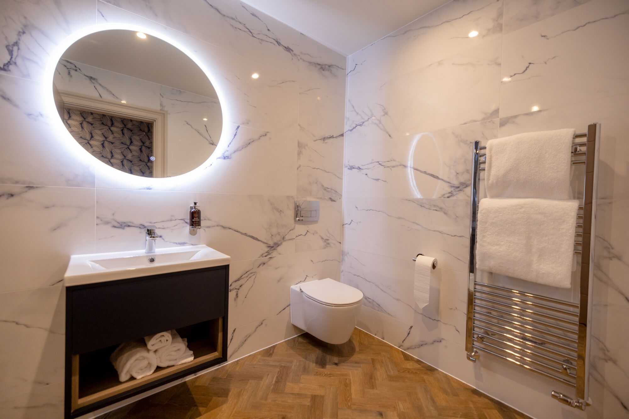 Un bagno moderno con un mobile lavabo in marmo, un water, una cabina doccia in vetro e un porta asciugamani.
