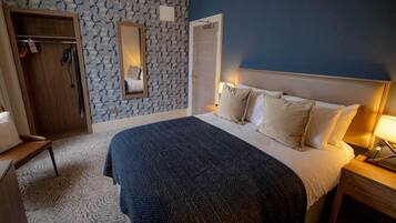 A hotel room with a bed, a bedside table, a nightstand, a wardrobe, a mirror, and a door.