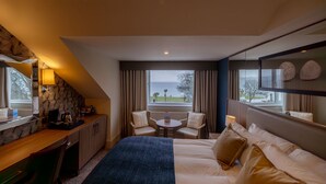 Une chambre d’hôtel avec un lit, un bureau, une chaise, une petite table et une vue sur la mer.