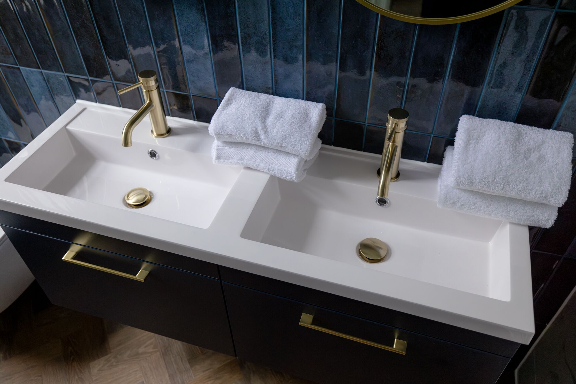 Une salle de bain avec un lavabo blanc, deux robinets dorés et un miroir au-dessus. Deux serviettes sont pliées et posées sur le lavabo.