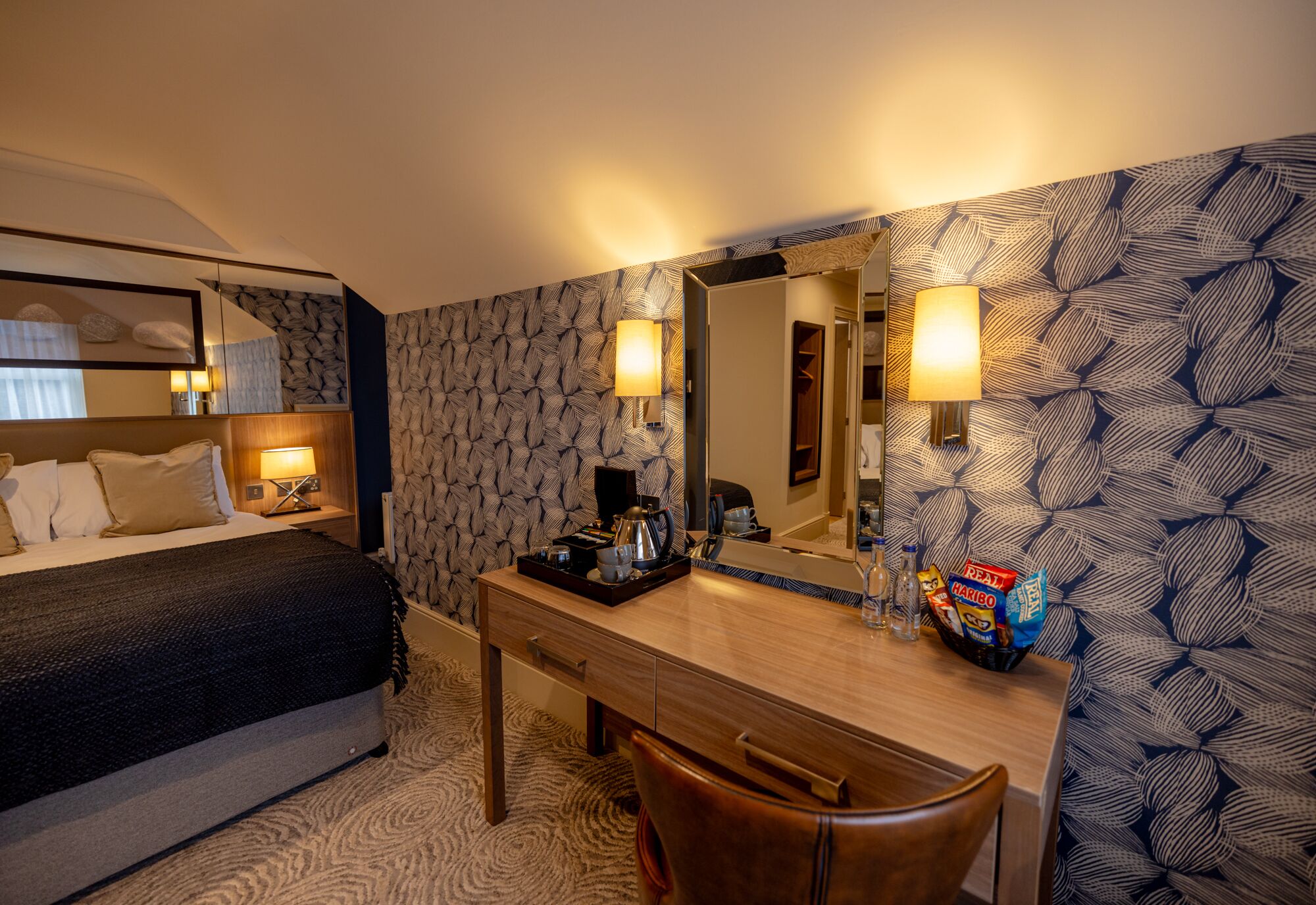 Ett hotellrum med en säng, ett skrivbord, en stol, en spegel och en vägg med ett mönster.