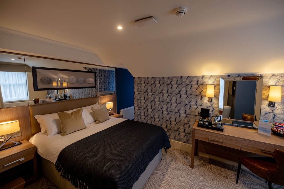 A hotel room with a bed, bedside table, dresser, and a mirror.