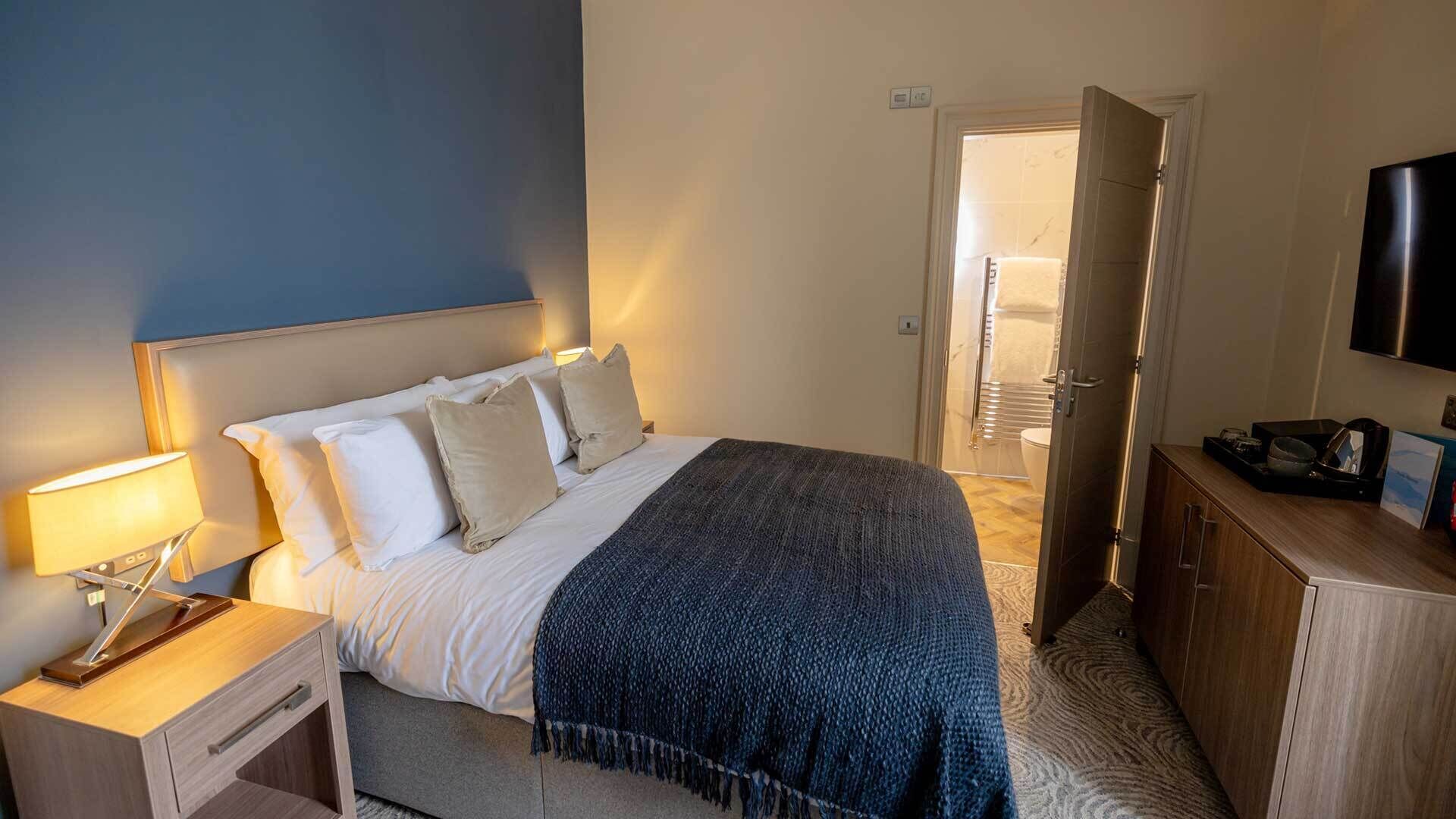Une chambre d’hôtel avec un lit, une table de chevet, une lampe et un téléviseur fixé au mur.