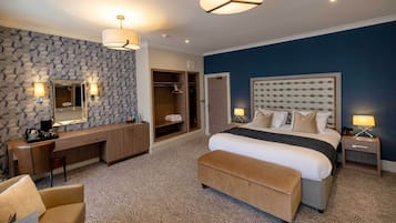 Una habitación de hotel moderna con una cama grande, un vestidor, un tocador con espejo y un área de descanso con una silla.