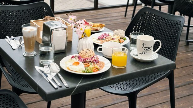 A dining table set with breakfast items, including eggs, toast, and fruit, in a restaurant with large windows and outdoor seating. - Old Mill Hotel (Klaipeda)