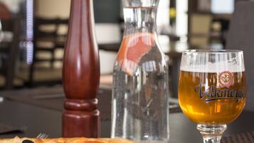 Una pizza con ingredientes, una cerveza en un vaso y un molinillo de pimienta sobre una mesa.