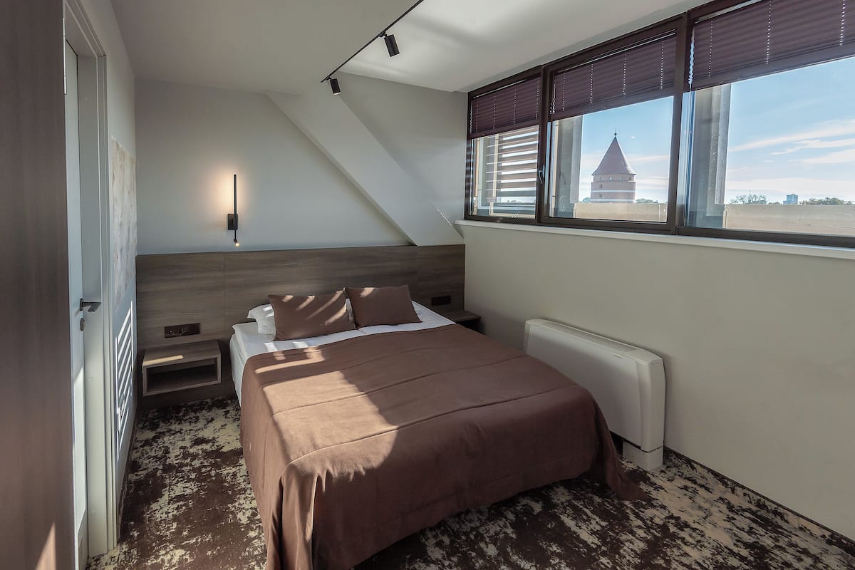 Ein Schlafzimmer mit einem Bett, Nachttischen, einem Fenster mit Jalousien und einer Heizung.