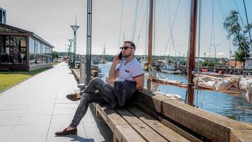 A man sitting on a wooden bench by a waterfront, talking on a phone.