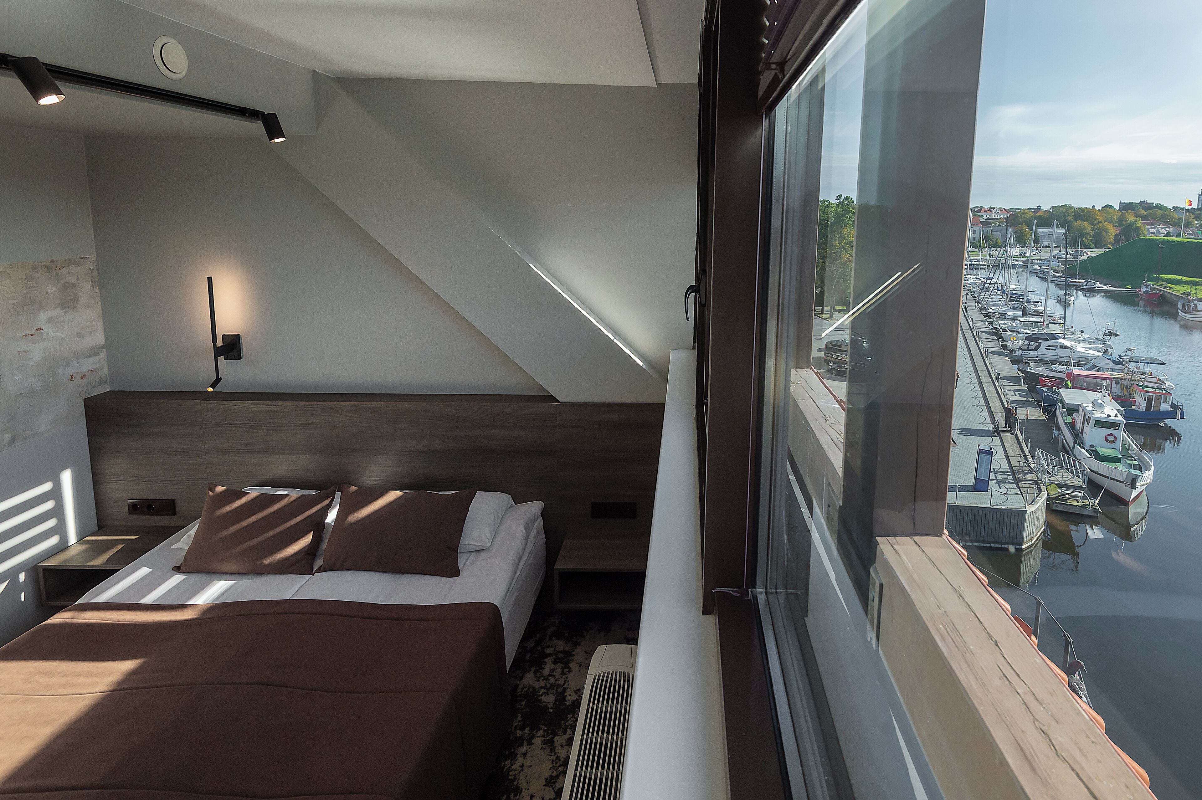 A modern bedroom with a bed, bedside table, and a view of a marina.