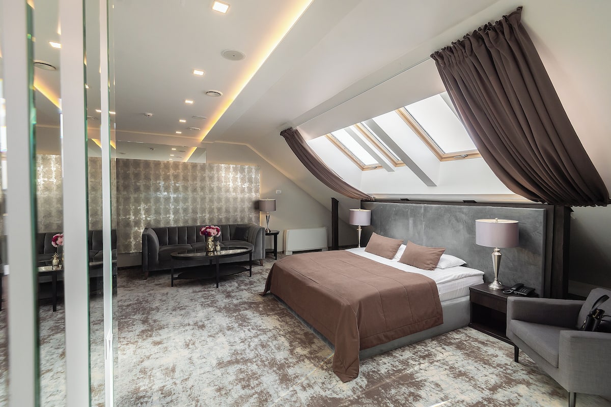 Ein modernes Hotelzimmer mit einem großen Bett, einer Couch, einem kleinen Tisch und einem Sessel. Über dem Bett befindet sich ein Oberlicht und es bietet sich ein Blick auf den Himmel.