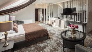 A modern hotel room with a bed, a round glass table, a TV, and a bathroom visible through a glass partition. - Old Mill Hotel (Klaipeda)