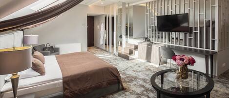 Une chambre d’hôtel moderne équipée d’un lit, d’une table ronde en verre, d’un téléviseur et d’une salle de bain visible à travers une paroi en verre.