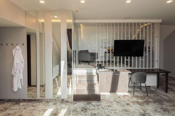 Un interior moderno con área de cocina, una mesa de comedor y un televisor de pantalla plana montado en un panel blanco.