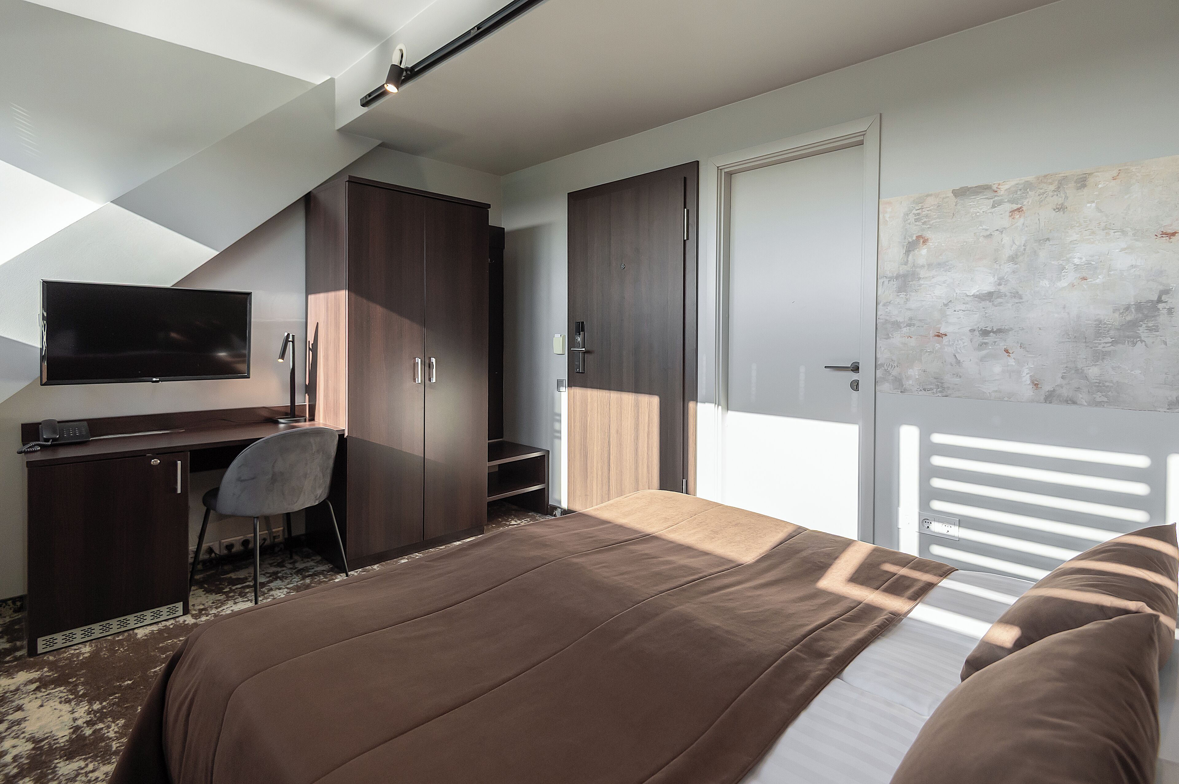 A bedroom with a bed, a desk, a chair, and a TV.