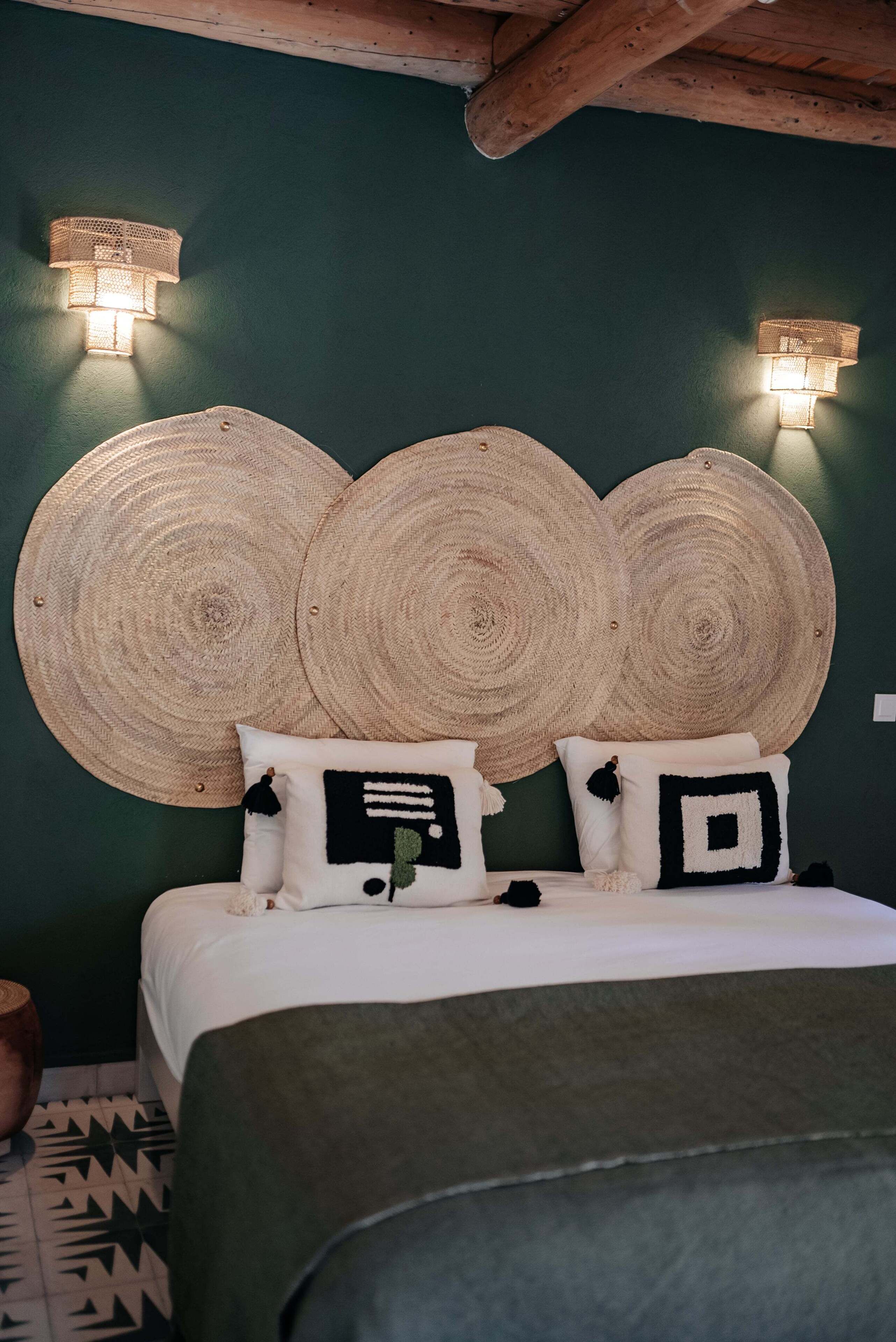 Una cama con cabecera verde, dos luces fijadas a la pared y un diseño de cabecera tejido.