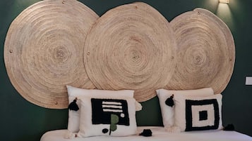 Una cama con cabecera verde, dos luces fijadas a la pared y un diseño de cabecera tejido.