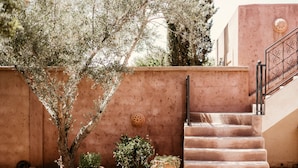 Un escalier menant à un bâtiment dont la façade est revêtue d’un matériau texturé, avec un pot de fleurs placé près des marches.