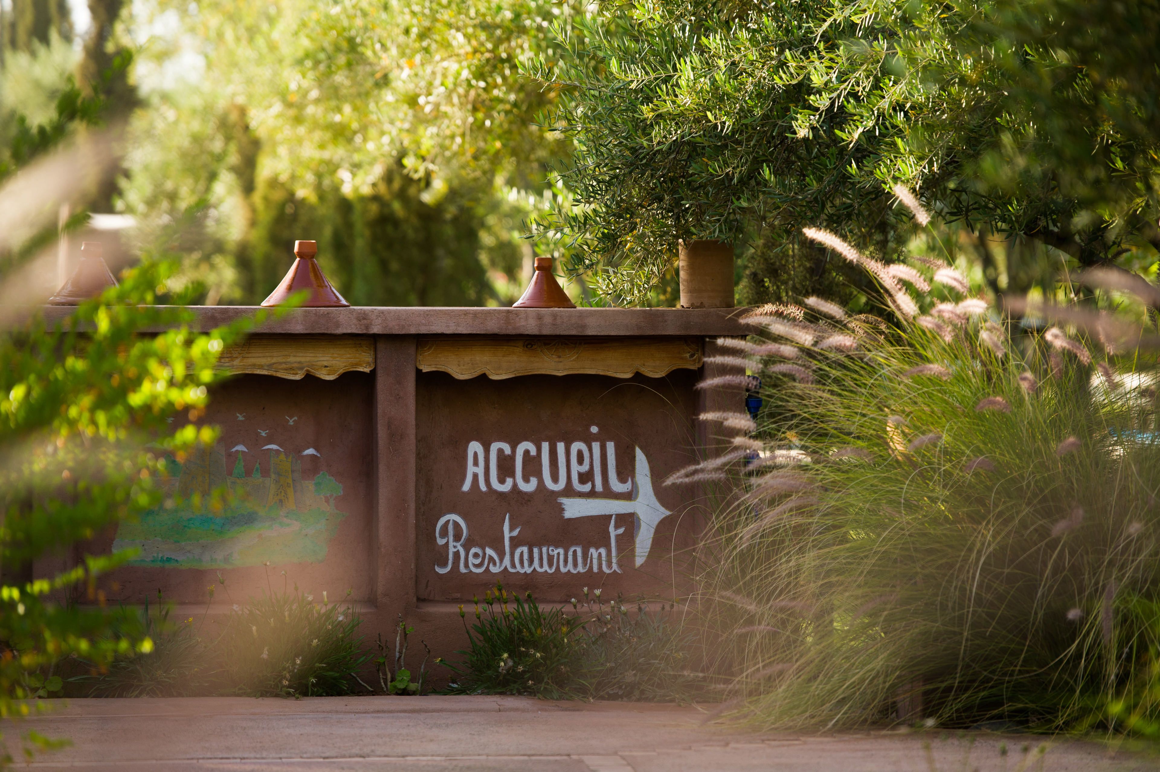 A rustic wall with a sign reading "Accueil Restaurant" and two clay pots on top.