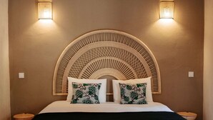 Une chambre à coucher avec une tête de lit incurvée, deux lampes de chevet, un lit recouvert d’une couverture noire et un banc en bois.