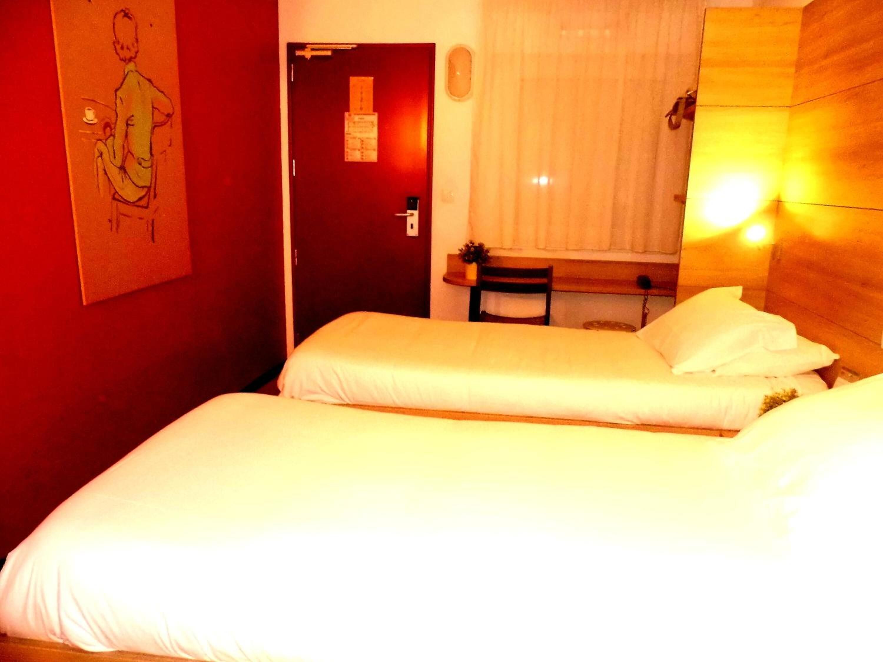 Ett hotellrum med två sängar, en sänggavel i trä, ett litet bord och en stol.
