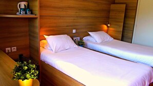 Une chambre d’hôtel avec deux lits simples, une tête de lit en bois, une petite table avec une plante et une étagère avec une machine à café.