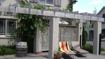 A house with a swimming pool, a covered patio with lounge chairs, and a large window with shutters.