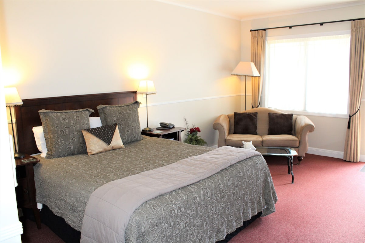 Ein Hotelzimmer mit einem großen Bett, einer Schlafcouch, einem kleinen Tisch und einem Fenster mit Vorhängen.