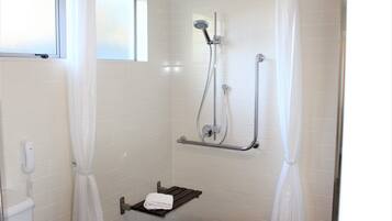 Un piccolo bagno rivestito di piastrelle bianche, con una doccetta, un portaservizi e una finestra.