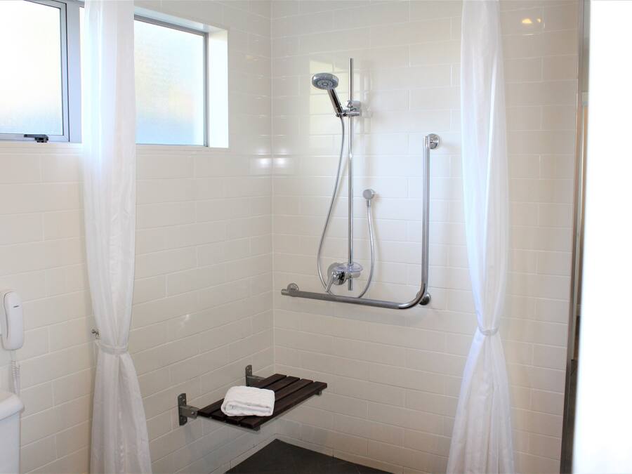 Un baño pequeño con paredes de azulejos blancos, un cabezal de ducha manual, un perchero y una ventana.