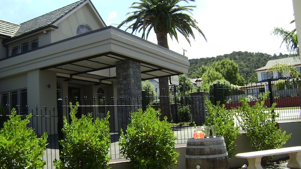 A modern house with a covered patio, stone pillars, and a fenced garden area with palm trees and shrubs. - Lodge Bordeaux (Whangarei)