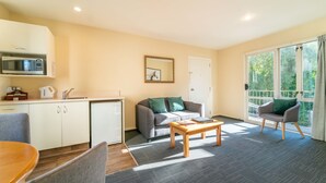Ein gemütlicher Wohnbereich mit Küchenzeile, einer Couch, einem Couchtisch und einem Sessel in der Nähe eines großen Fensters.