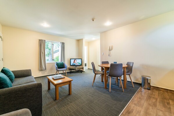 A modern living room with a sofa, a coffee table, a TV, and a dining area with chairs and a table. - City Centre Motel (Christchurch)