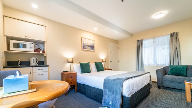 Ein Hotelzimmer mit einem Bett, einem Schlafsofa, einem Schreibtisch mit Stuhl, einer Mikrowelle, einem Wasserkocher und einem Bild an der Wand.