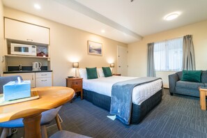 A hotel room with a bed, a sofa, a desk with a chair, a microwave, a kettle, and a painting on the wall. - City Centre Motel (Christchurch)