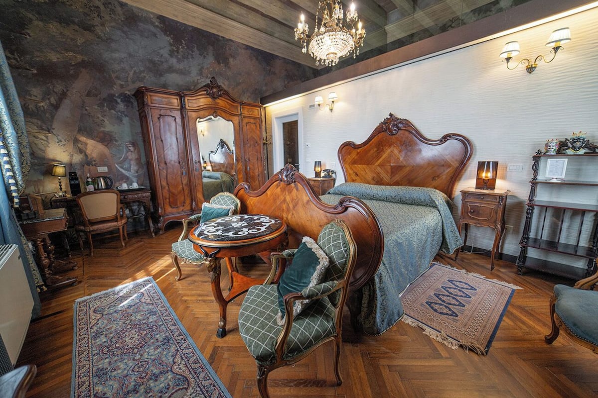 A vintage-style bedroom with a large bed, wooden furniture, and a chandelier.