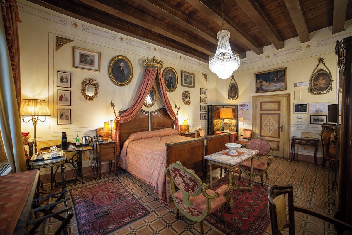 A traditional bedroom with a large bed, a chandelier, and a dining area with chairs and a table.