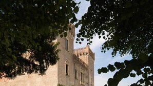 Un edificio histórico con una torre central, rodeado de jardines cuidados y un camino de grava.