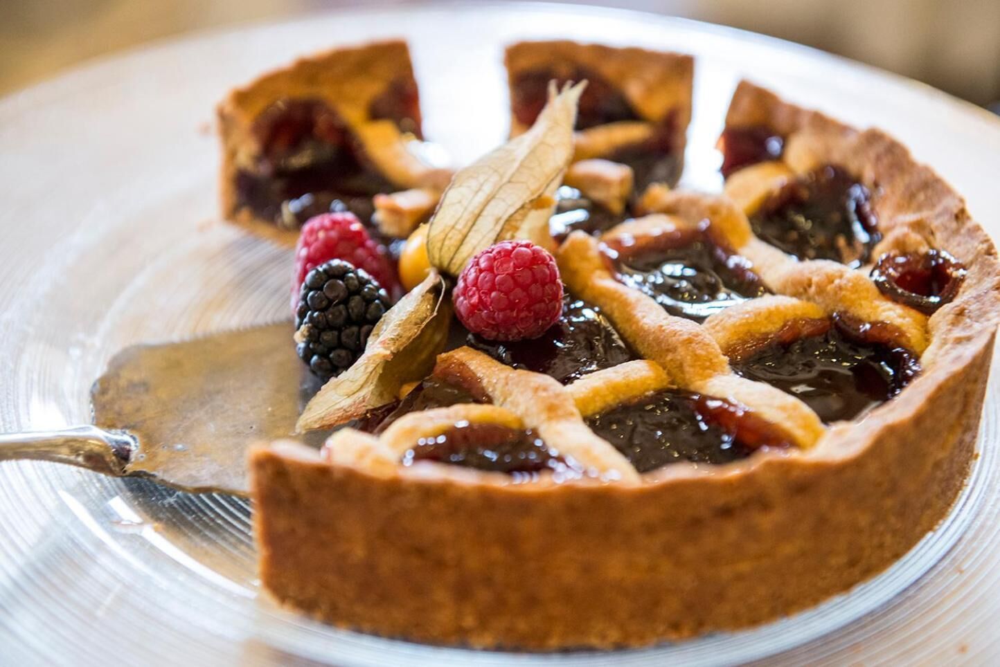 Una fetta di torta con frutti di bosco e una foglia decorativa su un piatto trasparente.