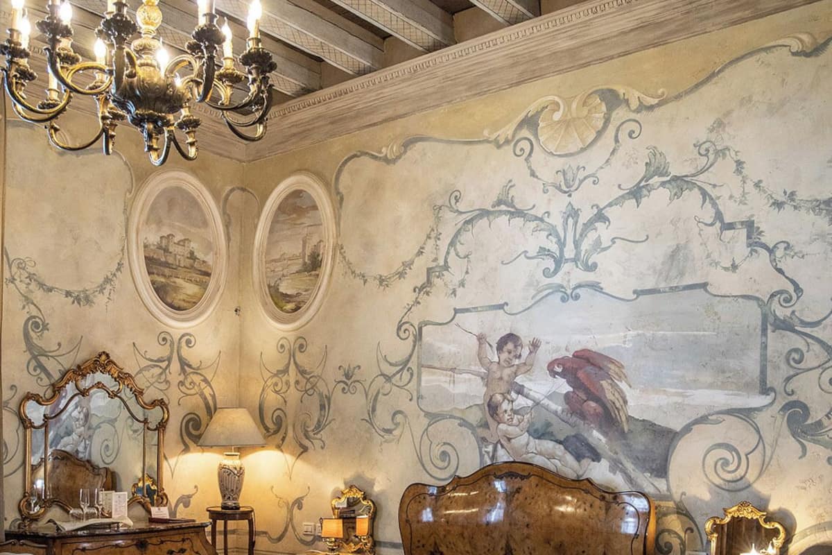 A classic bedroom with a wooden bed, ornate chandelier, and detailed wall murals.
