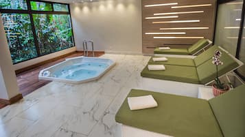 Un espace spa doté d’un jacuzzi, de sièges rembourrés de couleur verte et offrant une vue sur la verdure grâce à de grandes fenêtres.