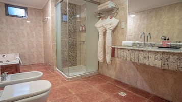 Ein modernes Badezimmer mit einer gläsernen Duschkabine, zwei Toiletten, einem Bidet und einem мраморных Fliesen Waschbecken mit Waschbecken und Handtuchhalter.
