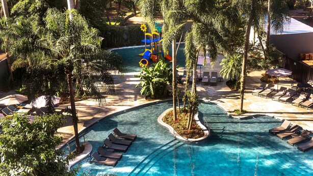 Uma área de piscina em resort, com espreguiçadeiras, palmeiras e um toboágua.