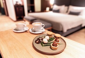 Bandeja de desayuno con pasteles y una taza de café sobre una mesa de madera en una habitación de hotel.