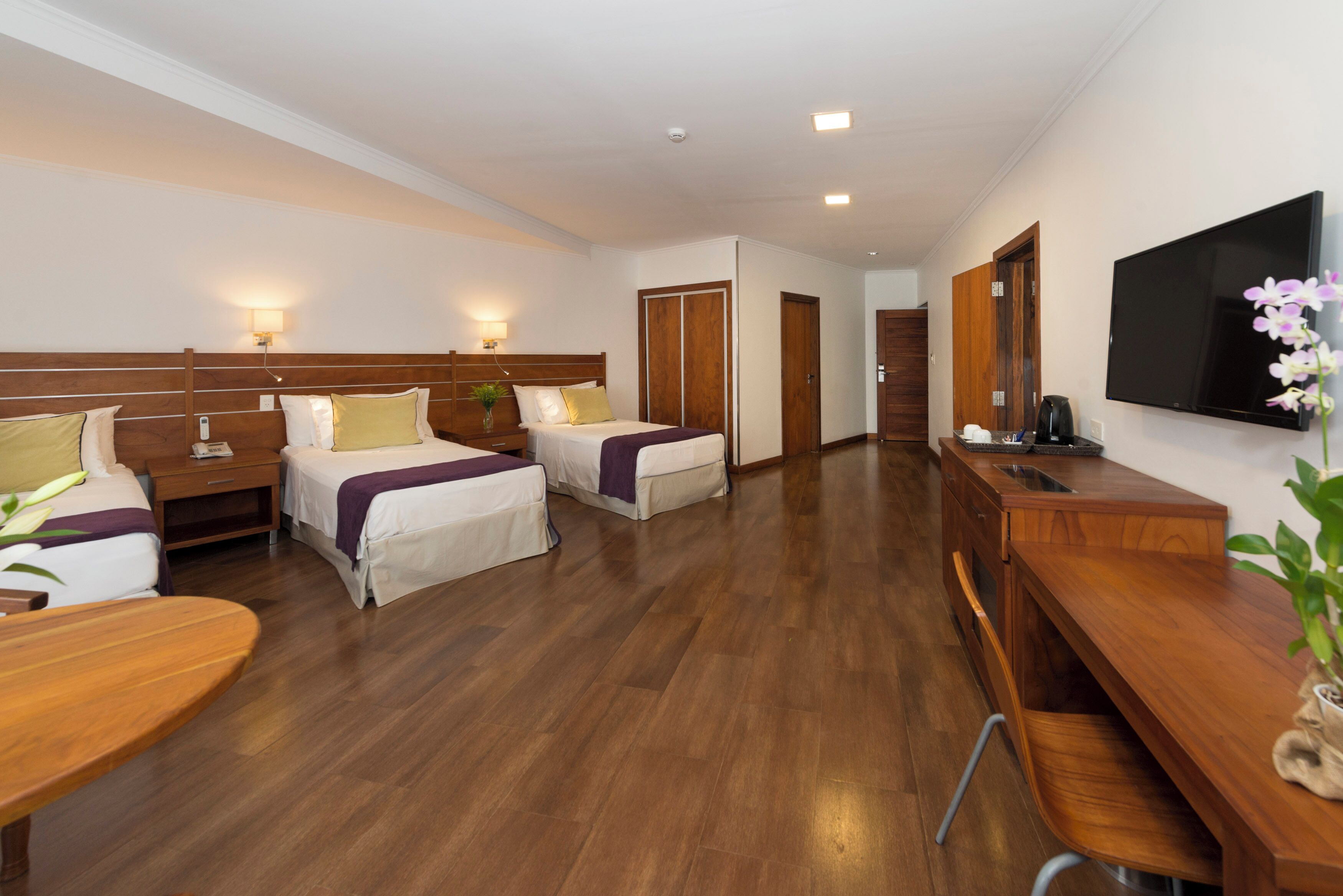 A hotel room with two beds, a desk, a TV, and a bathroom door.