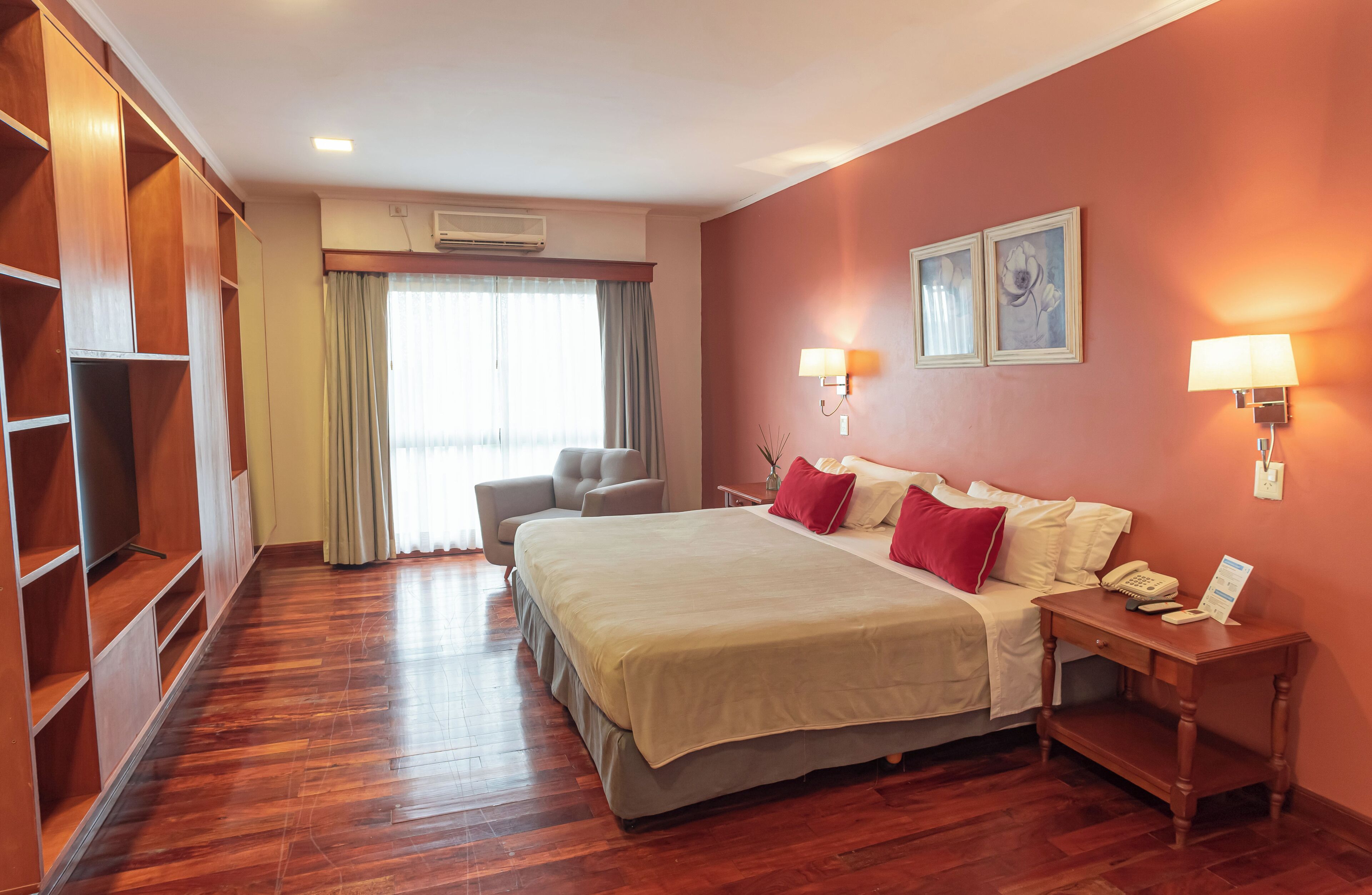 Habitación de hotel con una cama grande, un escritorio con teléfono, una silla, un armario y una ventana con cortinas.