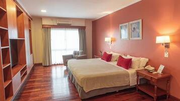 Habitación de hotel con una cama grande, un escritorio con teléfono, una silla, un armario y una ventana con cortinas.