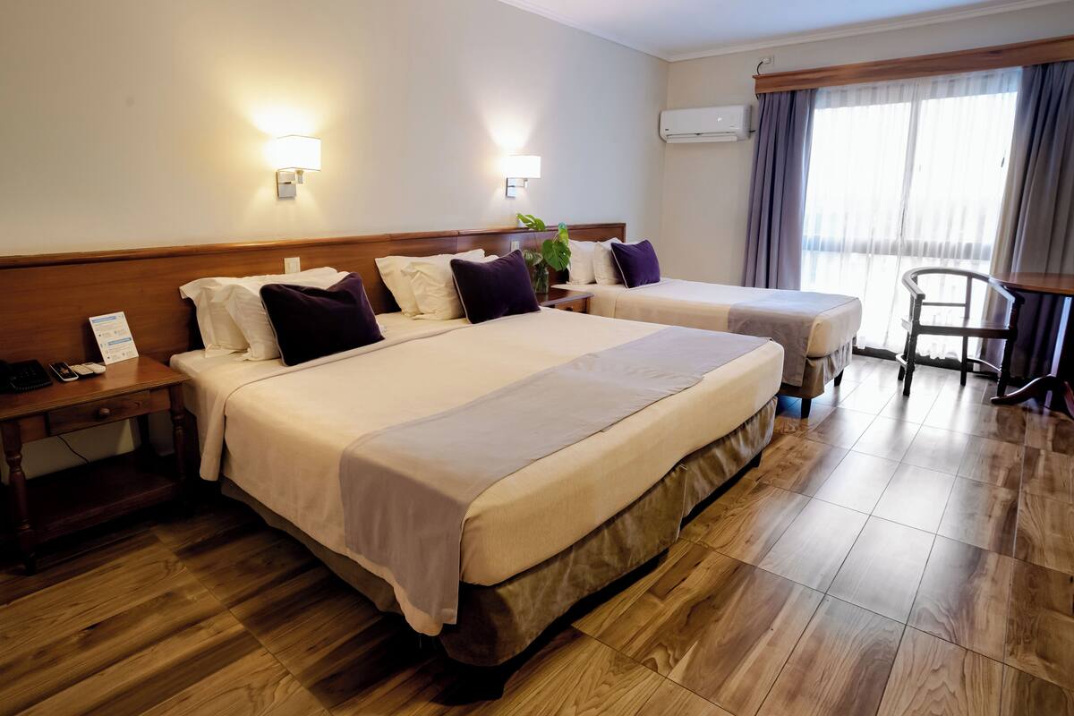 Ein Hotelzimmer mit zwei Betten, Holzboden, einem Schreibtisch mit Telefon und einem Stuhl.