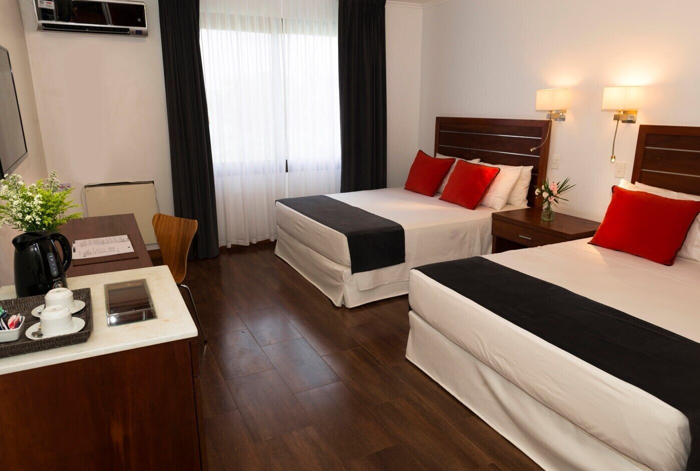 Habitación de hotel con dos camas, un escritorio, una cafetera y una ventana con cortinas.