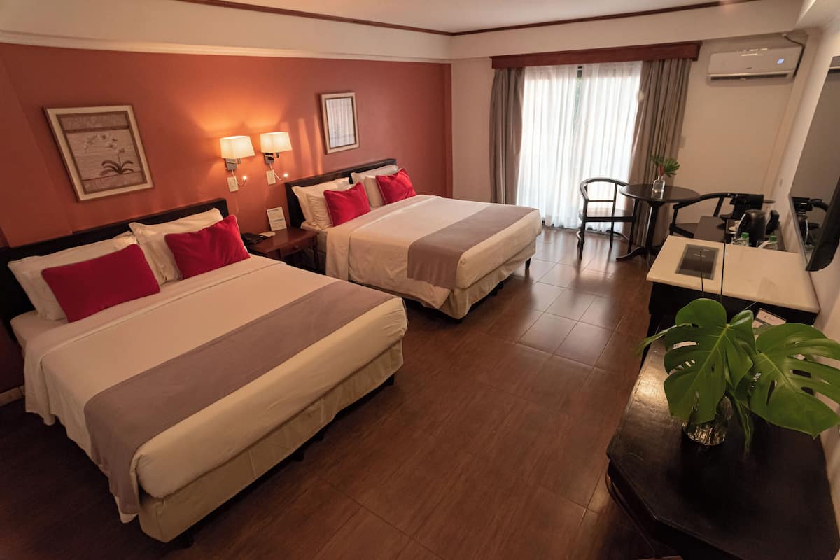 Ein Hotelzimmer mit zwei Betten, einem Schreibtisch, einem Stuhl und einer Topfpflanze.